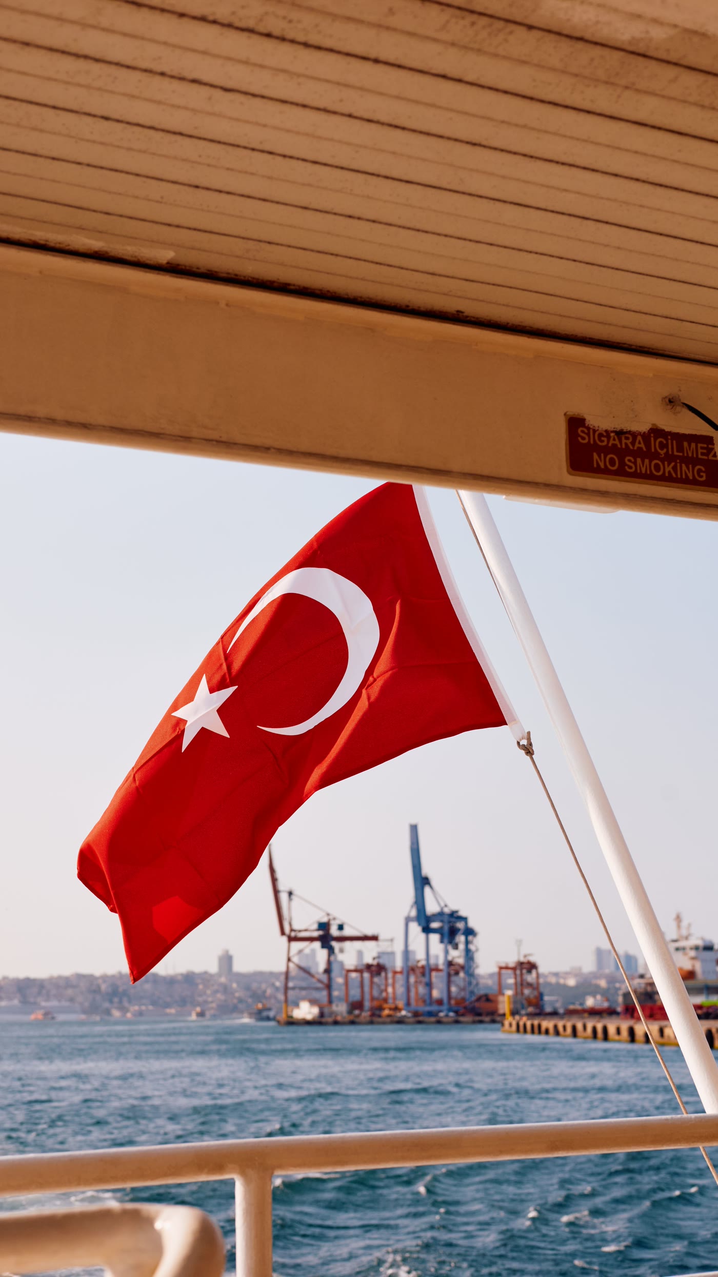 Turkish flag aboard a Bosphorus ferry with port cranes and the Istanbul skyline — AVANTI Global, marine commercial representation in Türkiye